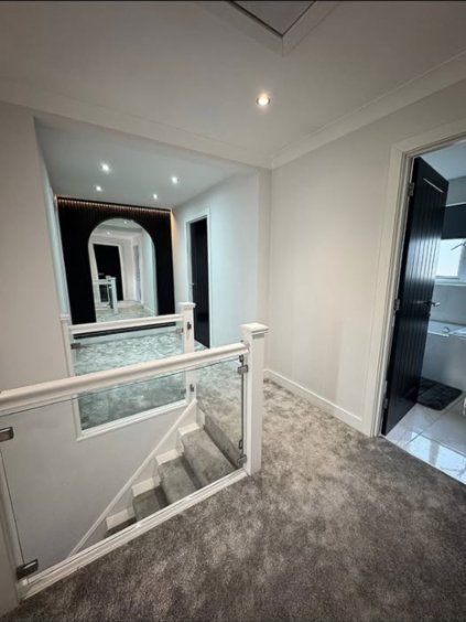New open landing with a glass balustrade, grey carpet and black doors